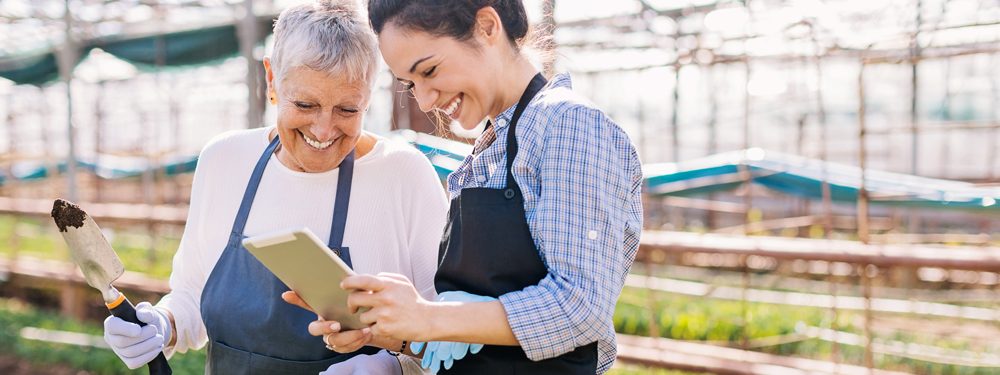 Mother and daughter look at a list on a tablet, whilst doing the gardening