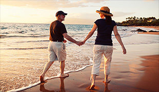 Couple in hats holding hand and walking in the surf of a beach funeral planning advice