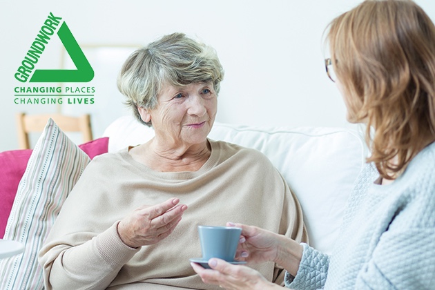 ground work logo with senior woman chatting to her daughter with a cup of tea on the sofa funeral plans