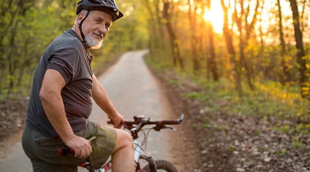 Senior man on a push bike with low sunlight, stopped and looking back