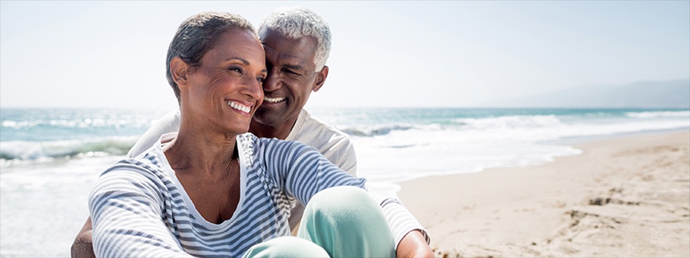 Senior couple cuddle and smile whilst sitting on beach