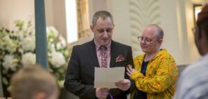 Man delivering a heartfelt eulogy at a funeral service, supported by a companion