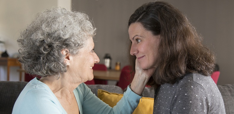 Happy senior mother touching face of beautiful daughter while talking to her. Middle-aged woman visiting mother. Family concept