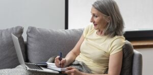 senior-woman-home-couch-using-laptop-taking-notes