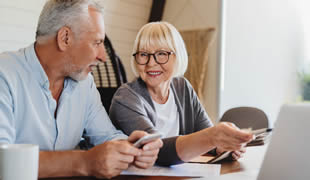 Older couple researching and discussing on their computer and mobile phone